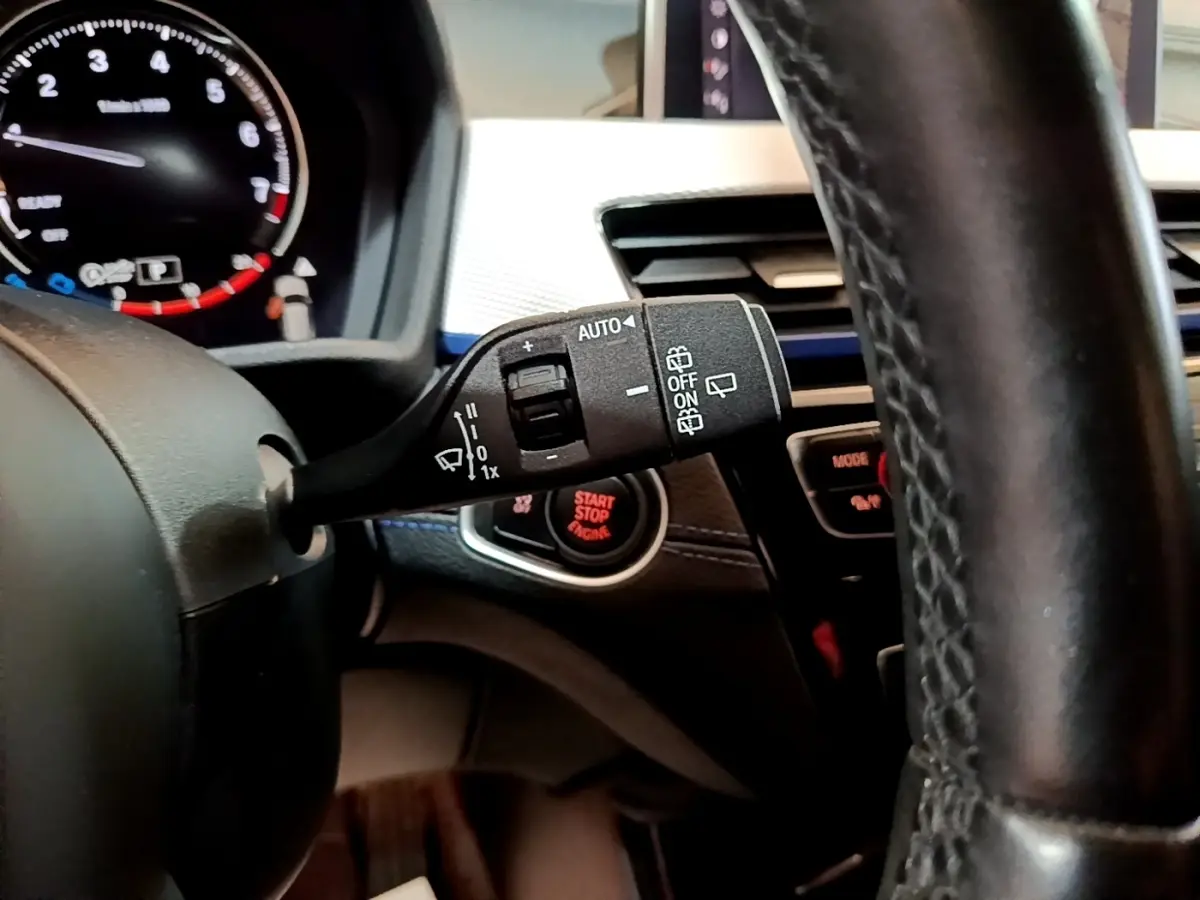 Gros plan sur la manette de commande d’essuie-glace à gauche du volant cuir noir dans l’habitacle du BMW X1 blanc 2022.