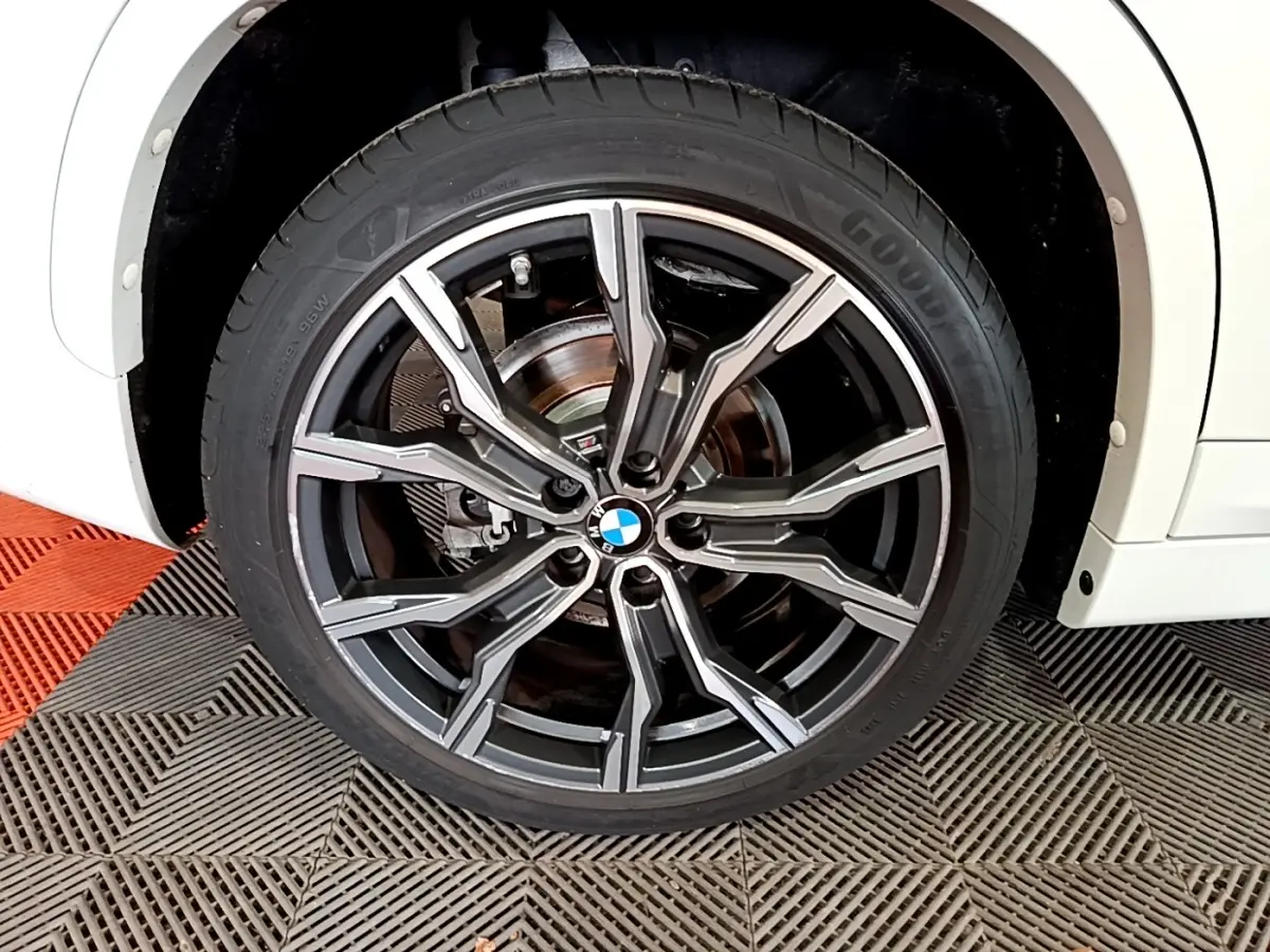 Gros plan sur la roue avant droite d’un BMW X1 blanc, jante alliage noire et argentée au design sportif.