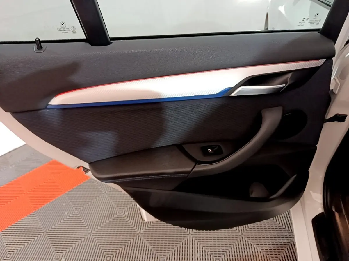 Vue rapprochée de la porte arrière droite blanche d’un BMW X1 2022 avec insert décoratif tricolore et poignée noire.