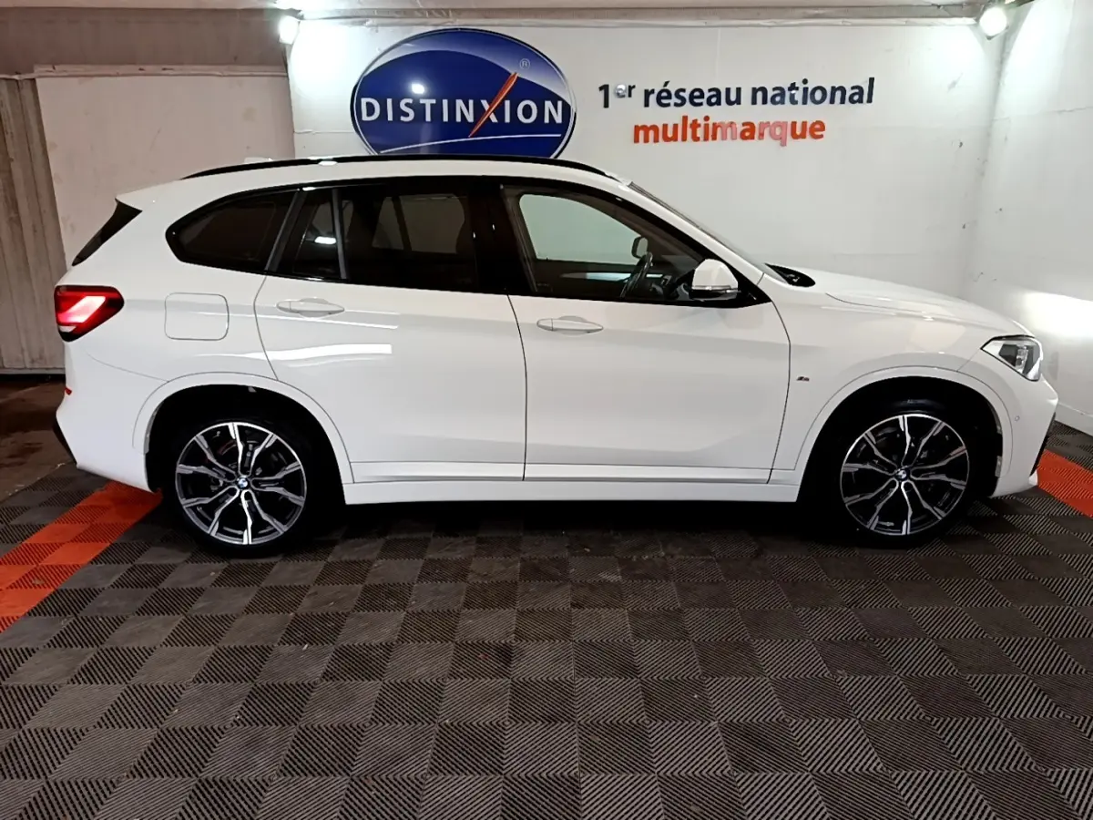 BMW X1 sDrive18i M Sport blanc vue de profil côté gauche, avec jantes alliage et feux arrière allumés.