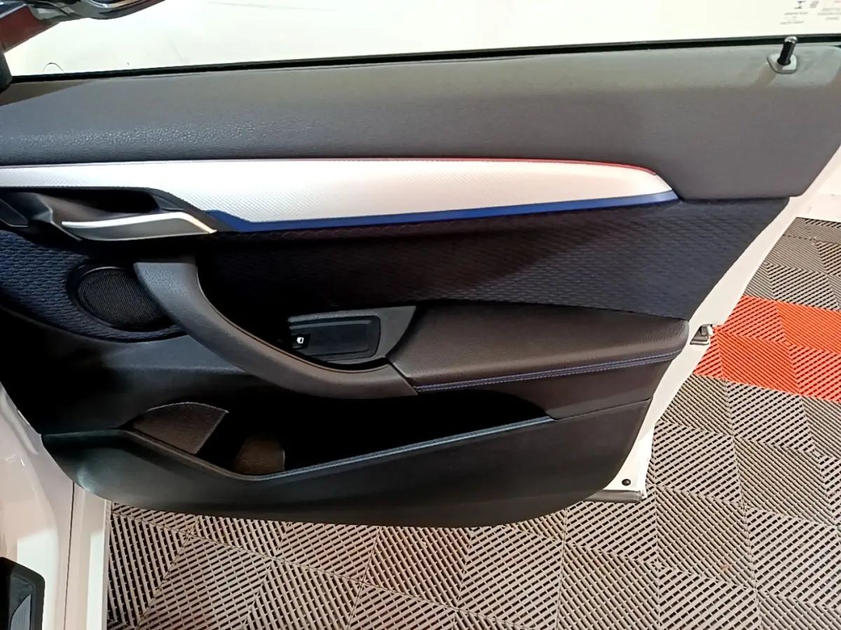 Vue rapprochée de la porte avant droite blanche du BMW X1 sDrive18i M Sport avec garniture noire et insert argenté.