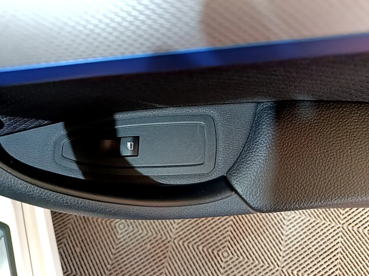 Gros plan sur le bouton de commande de lève-vitre côté conducteur d’un BMW X1 blanc, intérieur noir.