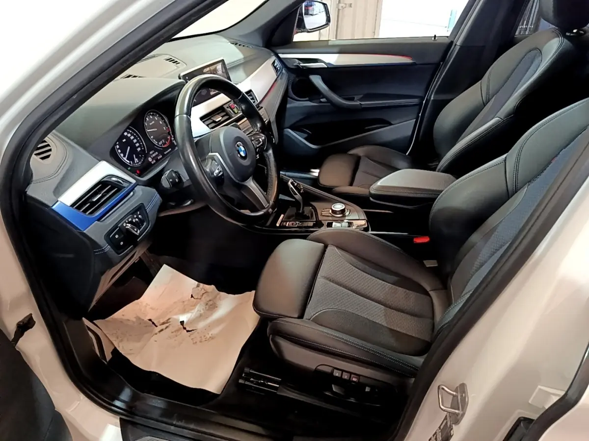 Vue intérieure côté conducteur de la BMW X1 blanc, montrant sièges noirs et tableau de bord avec écran tactile.