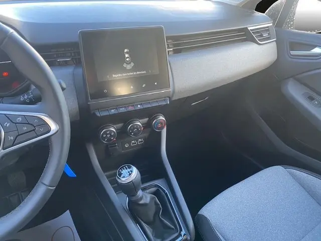 Vue intérieure côté passager avant de la Renault Clio V 1.5 DCI gris schiste, montrant la console centrale avec écran tactile et levier de vitesse manuel.