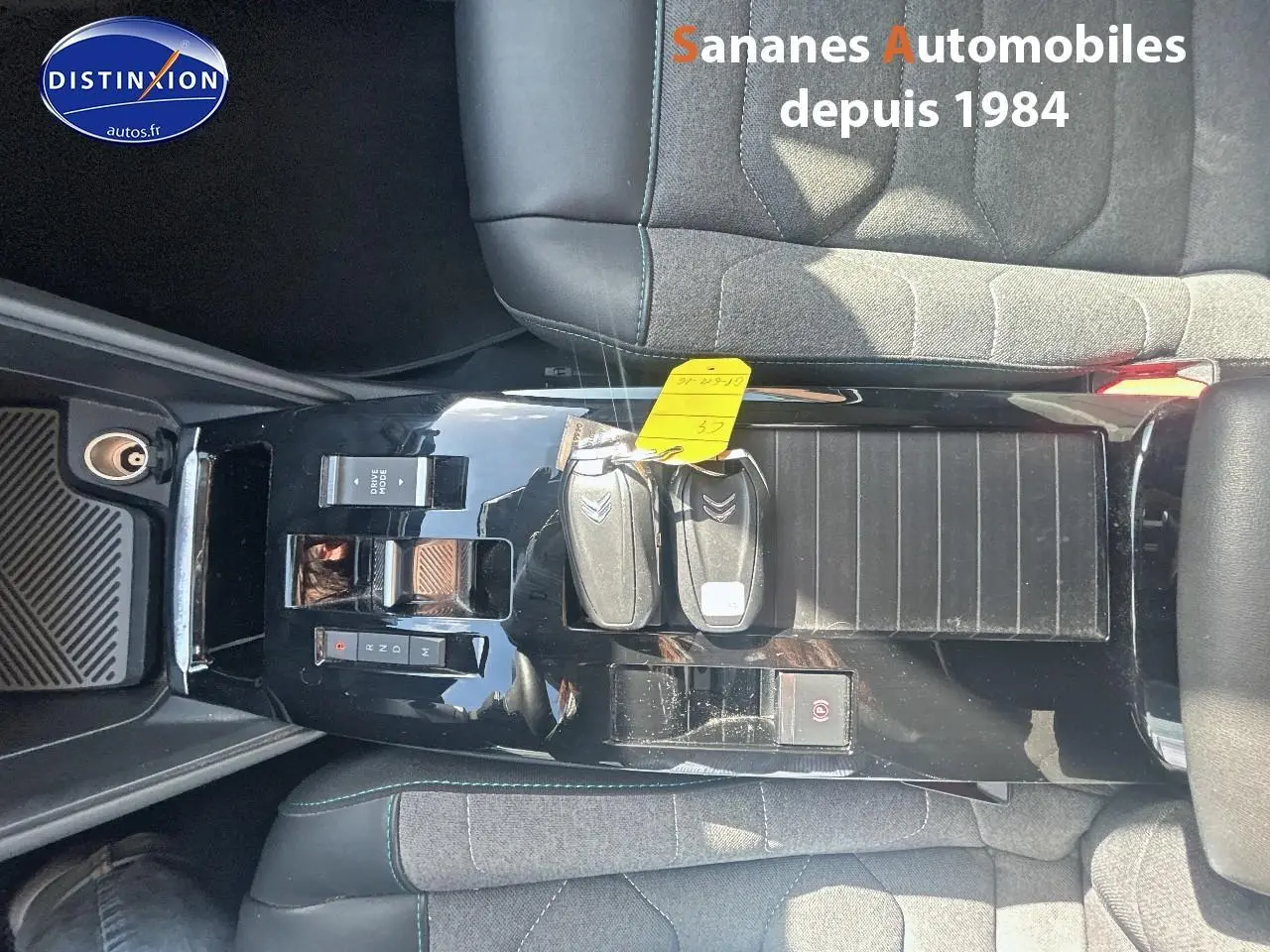 Vue plongeante sur la console centrale noire brillante de la Citroën C4 avec clés et sièges tissu gris et cuir noir.