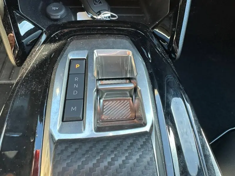 Gros plan sur la console centrale noire brillante du Peugeot 2008 1.2 Hybrid avec sélecteur de boîte automatique et bouton de mode.