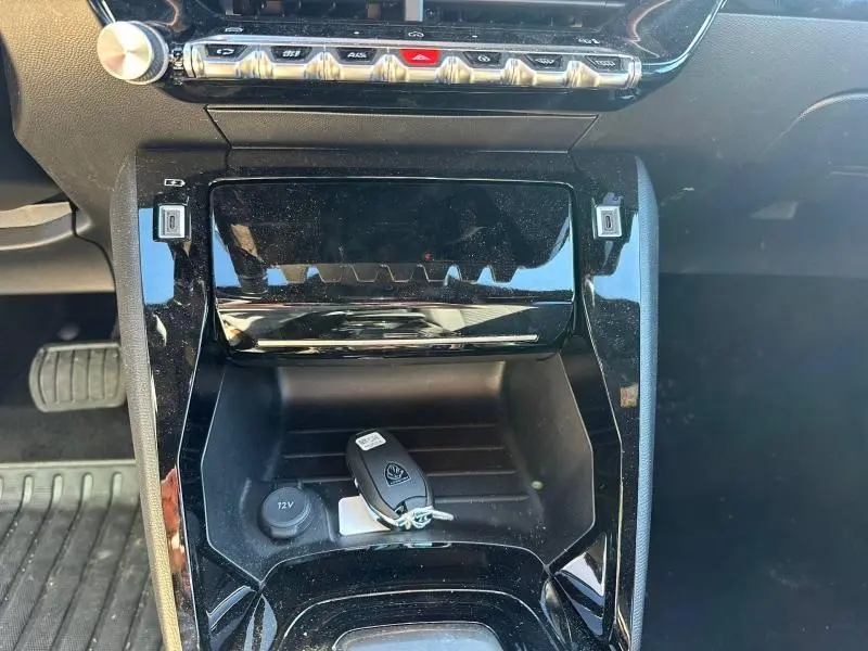 Gros plan sur la console centrale noire brillante du Peugeot 2008 1.2 Hybrid 145ch avec clé posée, intérieur moderne et épuré.