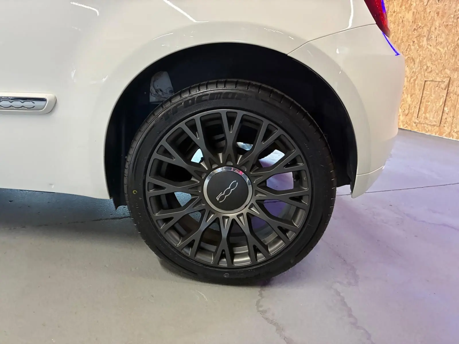 Gros plan sur la roue arrière droite d'une FIAT 500 blanc crème, mettant en valeur la jante noire au design complexe.
