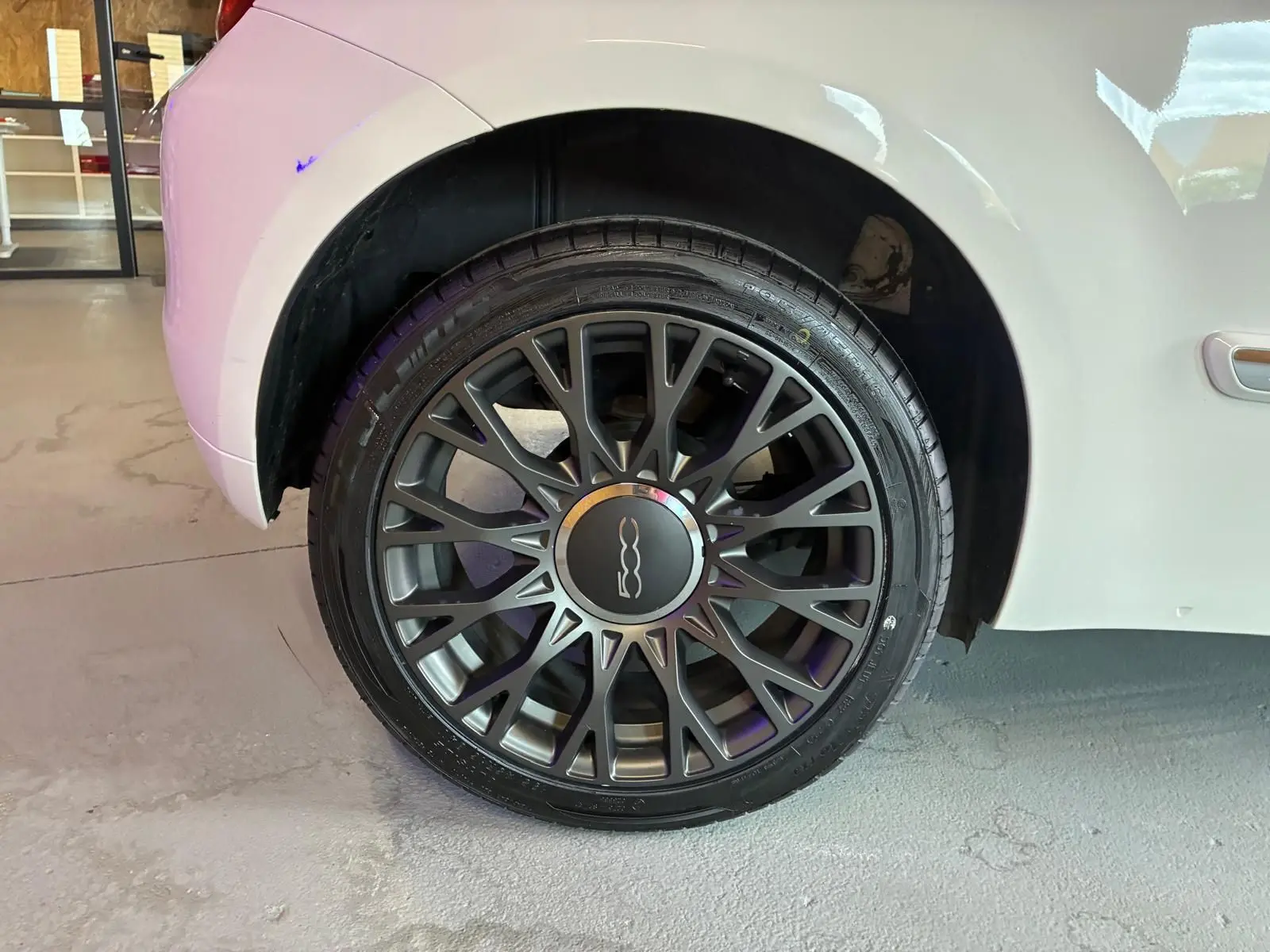 Gros plan sur la roue arrière droite d'une FIAT 500 blanc crème, mettant en valeur la jante noire à multiples branches.