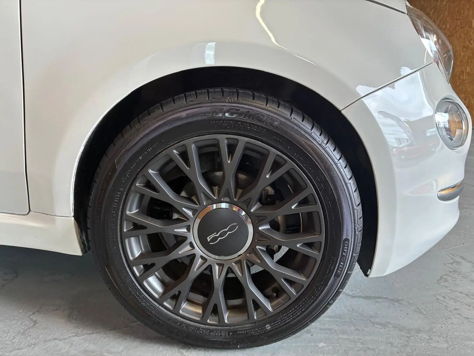Gros plan sur la roue avant droite d'une FIAT 500 blanc crème, mettant en valeur la jante foncée au design ajouré.