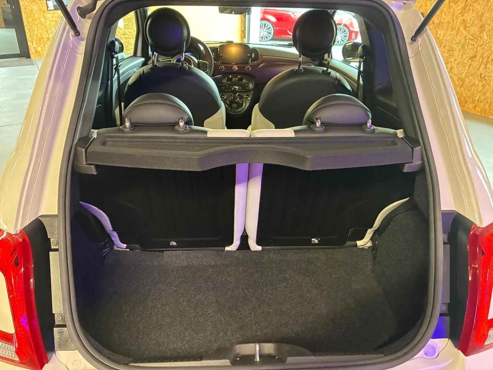 Vue arrière ouverte du coffre d'une FIAT 500 blanc crème, avec intérieur noir et blanc visible jusqu'au tableau de bord.