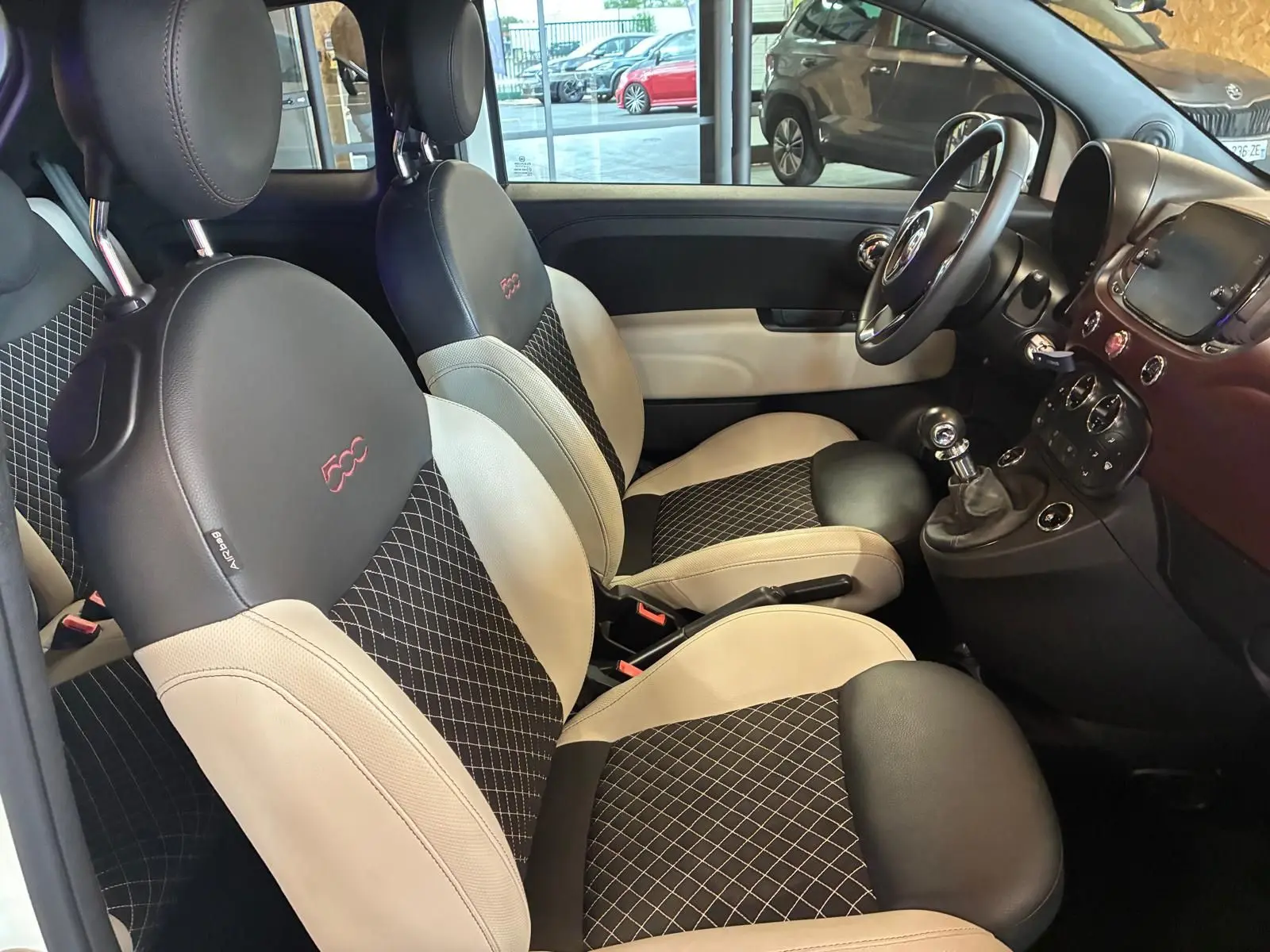 Vue intérieure côté conducteur de la Fiat 500 blanc crème, sièges noir et crème avec logo 500 brodé rouge.