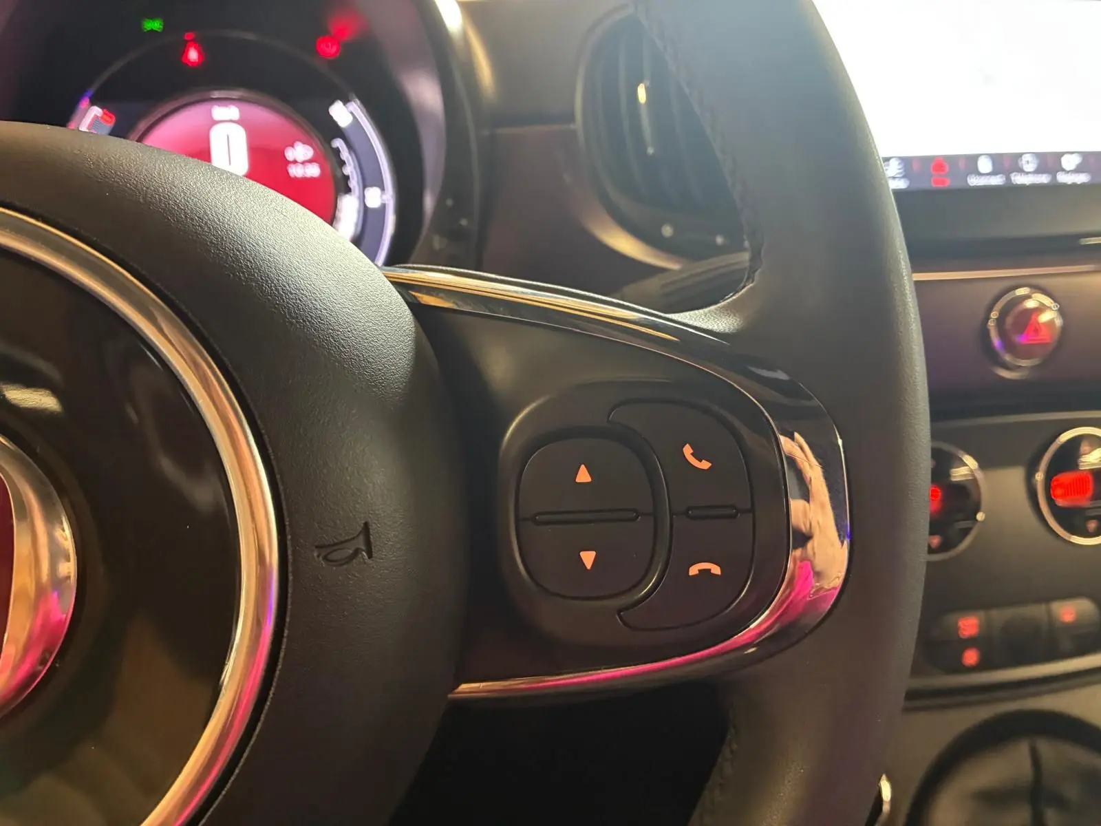 Gros plan sur le volant de la Fiat 500 blanc crème, avec commandes intégrées et tableau de bord lumineux en arrière-plan.