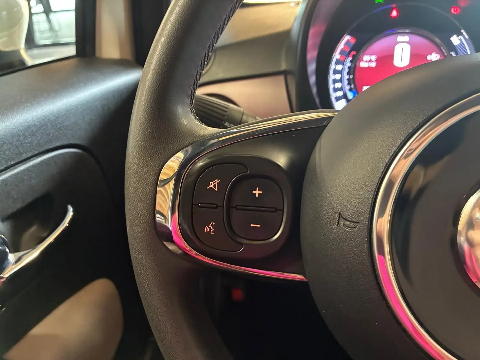 Gros plan sur le volant côté gauche d’une Fiat 500 blanc crème, montrant les commandes audio intégrées.