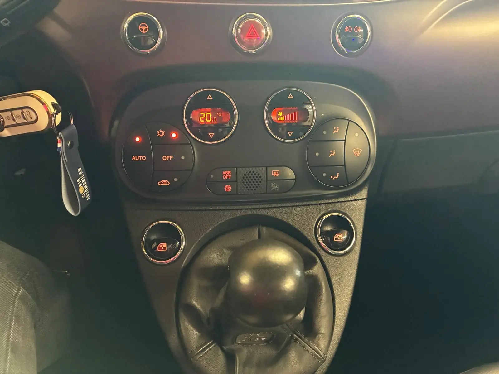 Vue rapprochée du levier de vitesses manuel et du tableau de commande de climatisation d’une Fiat 500 crème 2021.