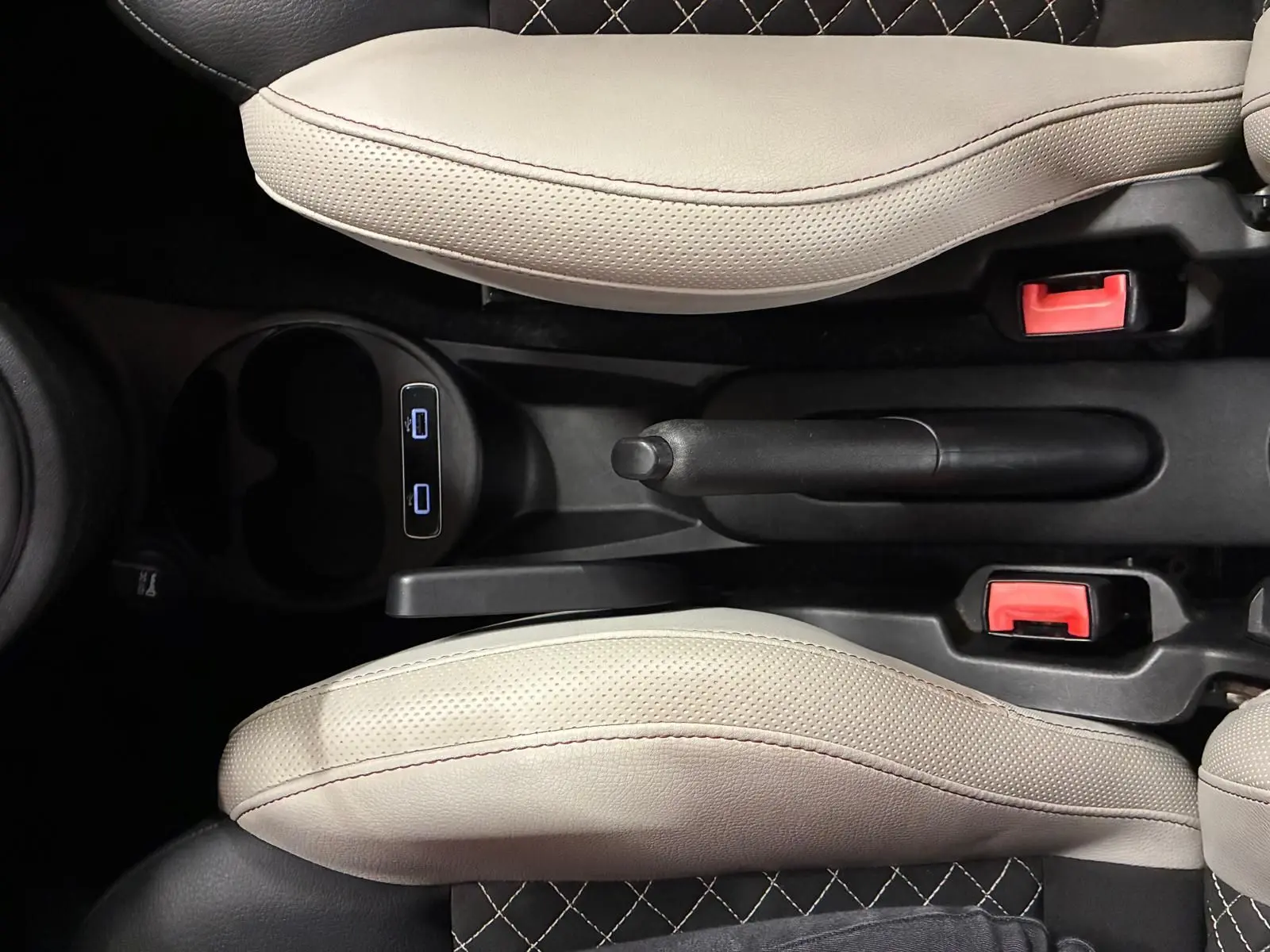 Vue plongeante sur la console centrale du Fiat 500 blanc crème, montrant frein à main et sièges en cuir bicolore noir et crème.
