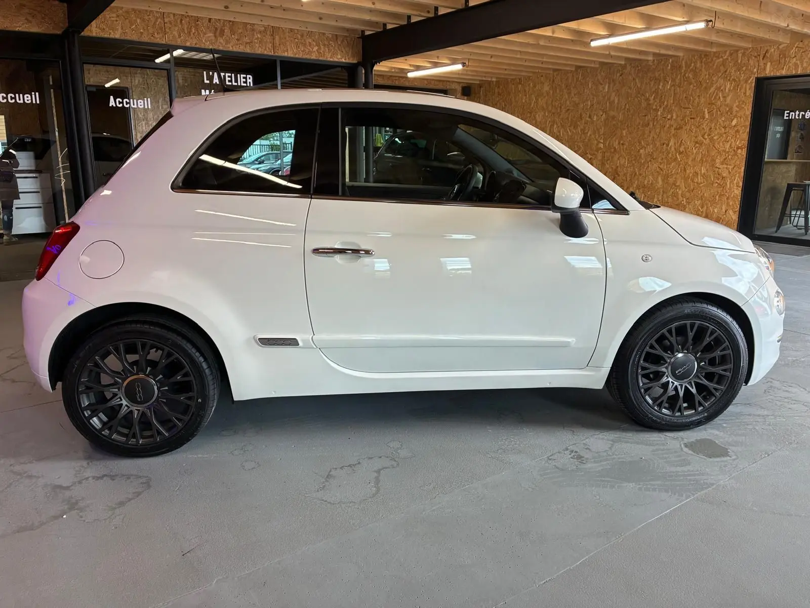 Vue de profil côté gauche d'une FIAT 500 blanc crème avec jantes noires en intérieur d'atelier.