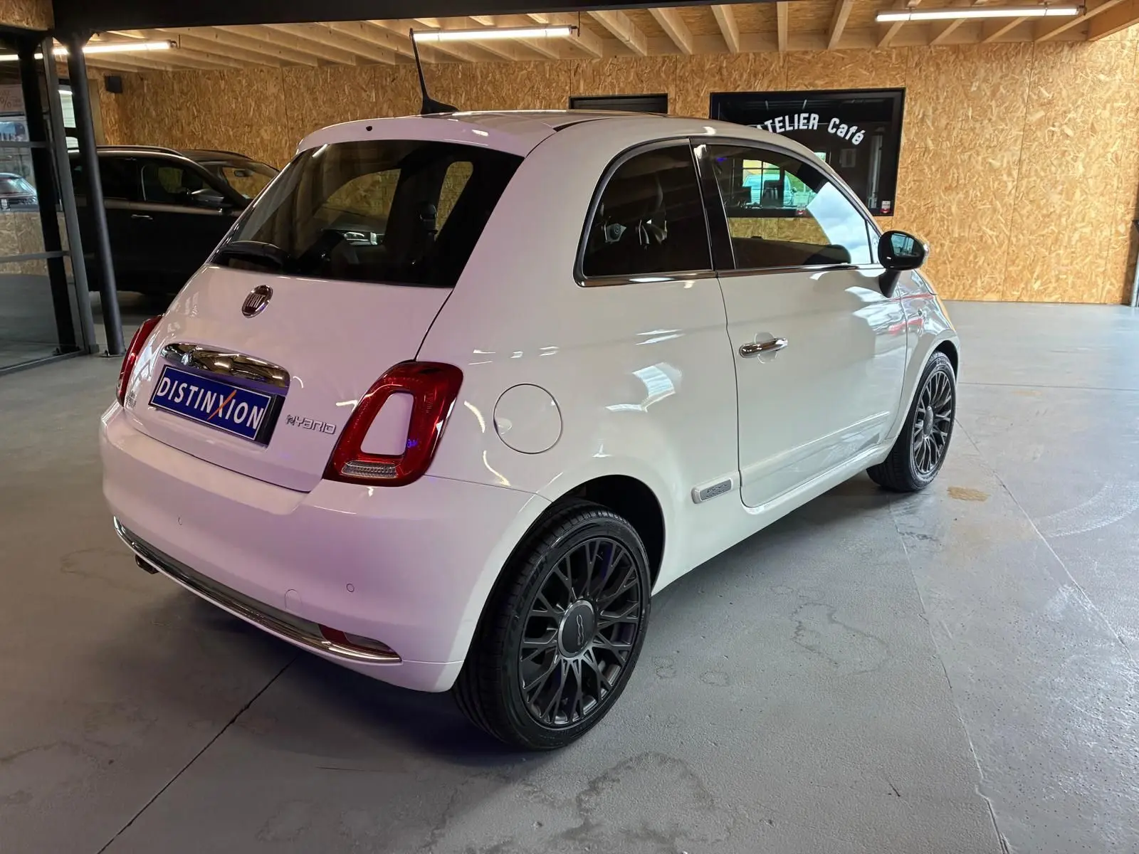 Vue 3/4 arrière droite d'une Fiat 500 blanc crème avec jantes noires et détails chromés dans un garage.