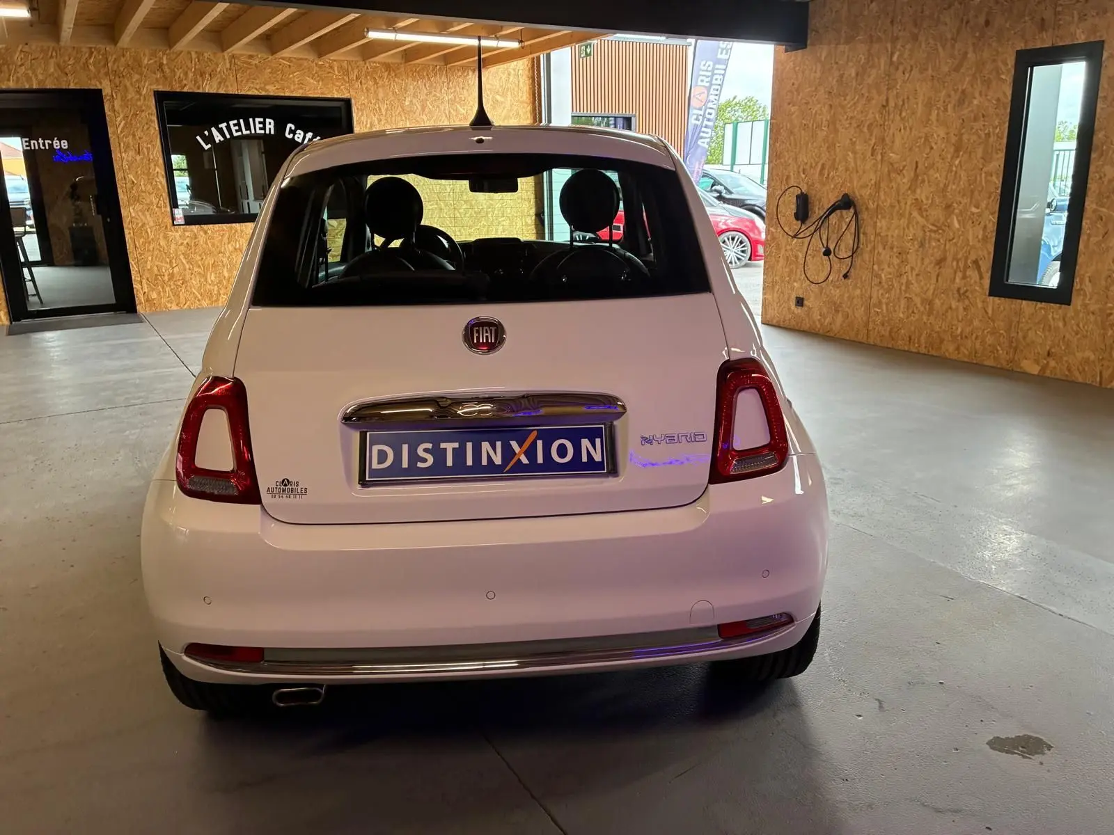 Vue arrière d'une FIAT 500 blanc crème hybride, stationnée en intérieur avec plaque Distinxion visible.