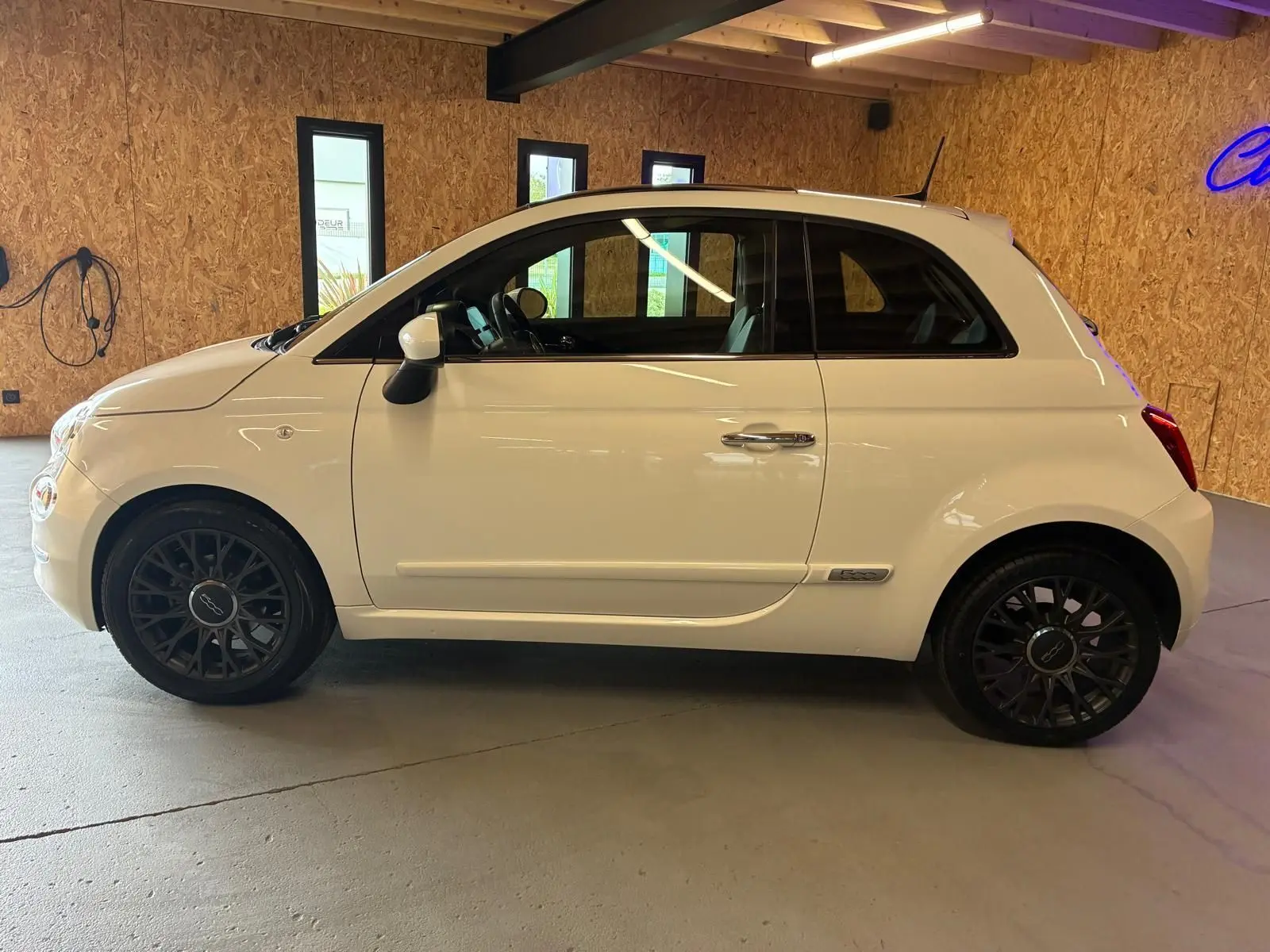 Vue de profil côté gauche d'une FIAT 500 blanc crème 2021 avec jantes noires et intérieur visible.