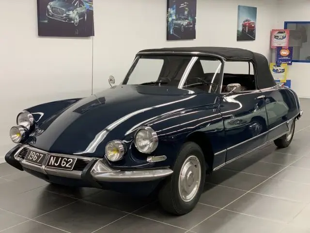 Vue 3/4 avant d'une Citroën DS3 Cabriolet Chapron 1967 bleu marine avec capote noire en intérieur showroom.