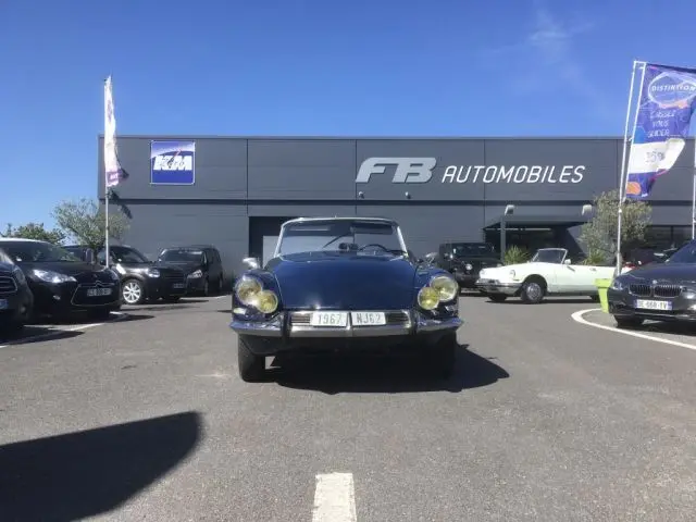 Vue frontale d'une Citroën DS3 DS21 Cabriolet Chapron bleu marine de 1967, capote baissée, sur un parking extérieur.