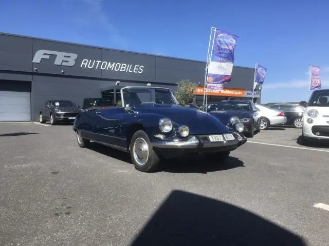 Citroën DS3 Cabriolet Chapron bleu marine vu en 3/4 avant droit sur parking devant concession automobile.