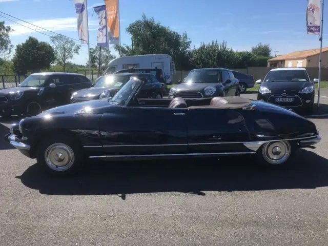Profil côté gauche d'une Citroën DS3 Cabriolet Chapron bleu marine de 1967 avec capote beige baissée, en extérieur.