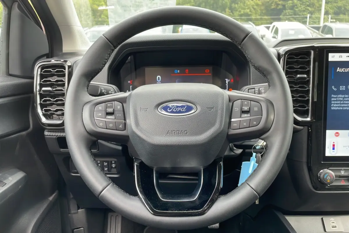 Vue rapprochée du volant noir du Ford Ranger 2025 avec commandes intégrées et tableau de bord numérique.