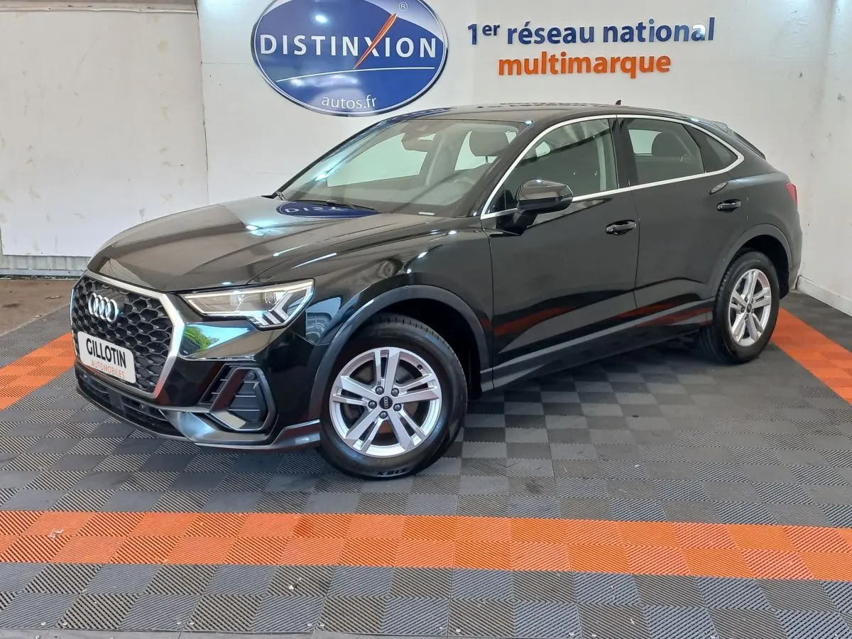Audi Q3 Sportback noir vue 3/4 avant droit, avec calandre hexagonale et jantes argentées en intérieur showroom.