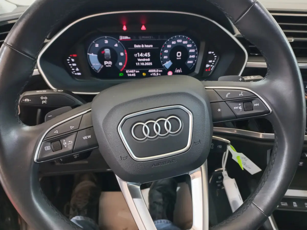 Vue rapprochée du volant cuir noir d'un Audi Q3 Sportback 35 TDI 150 S tronic avec tableau de bord numérique allumé.