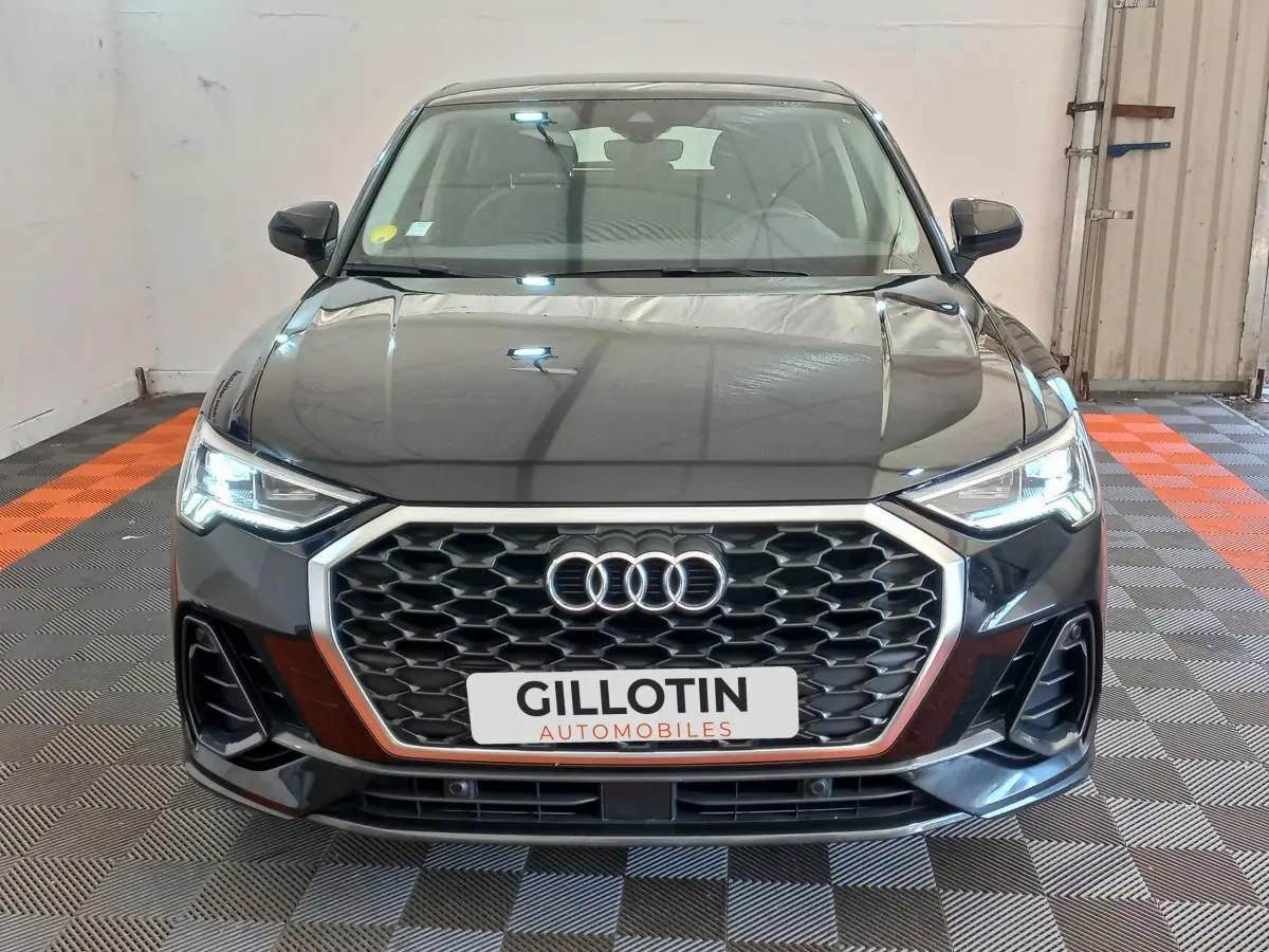 Audi Q3 Sportback noir vue de face, mettant en valeur sa calandre hexagonale et ses phares LED allumés.