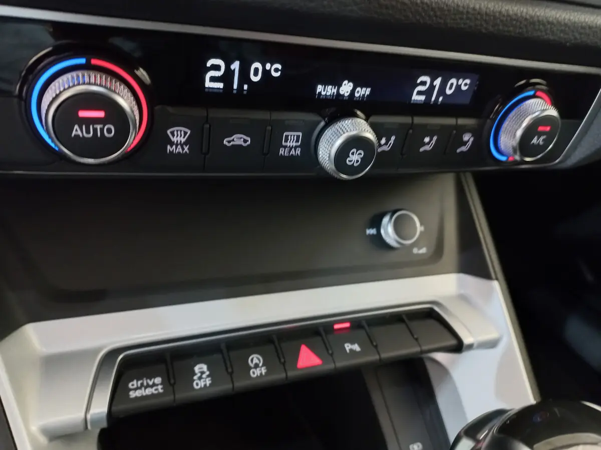 Gros plan sur la console centrale de l'Audi Q3 Sportback noire, affichant la climatisation digitale à 21°C.