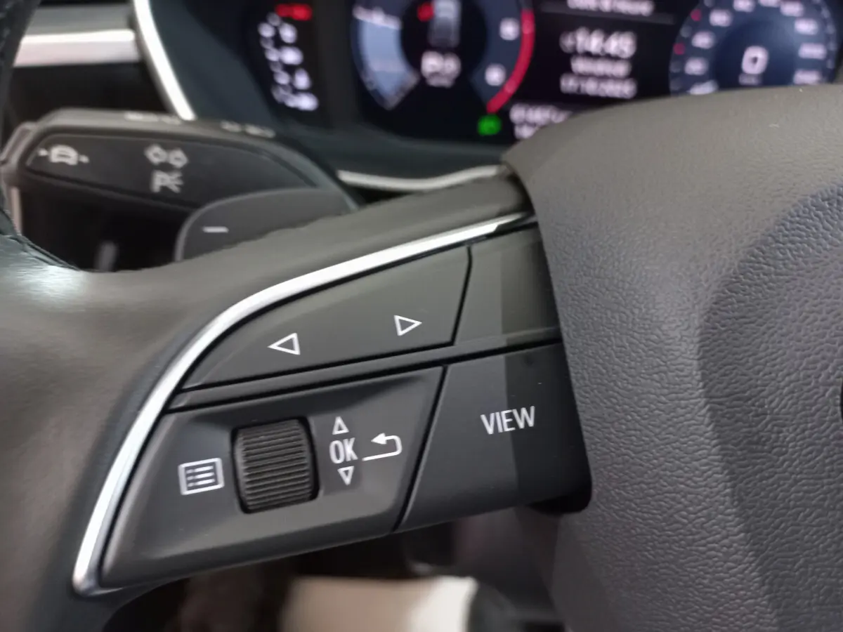 Gros plan sur les commandes gauche du volant cuir d'un Audi Q3 Sportback noir, avec affichage numérique en arrière-plan.