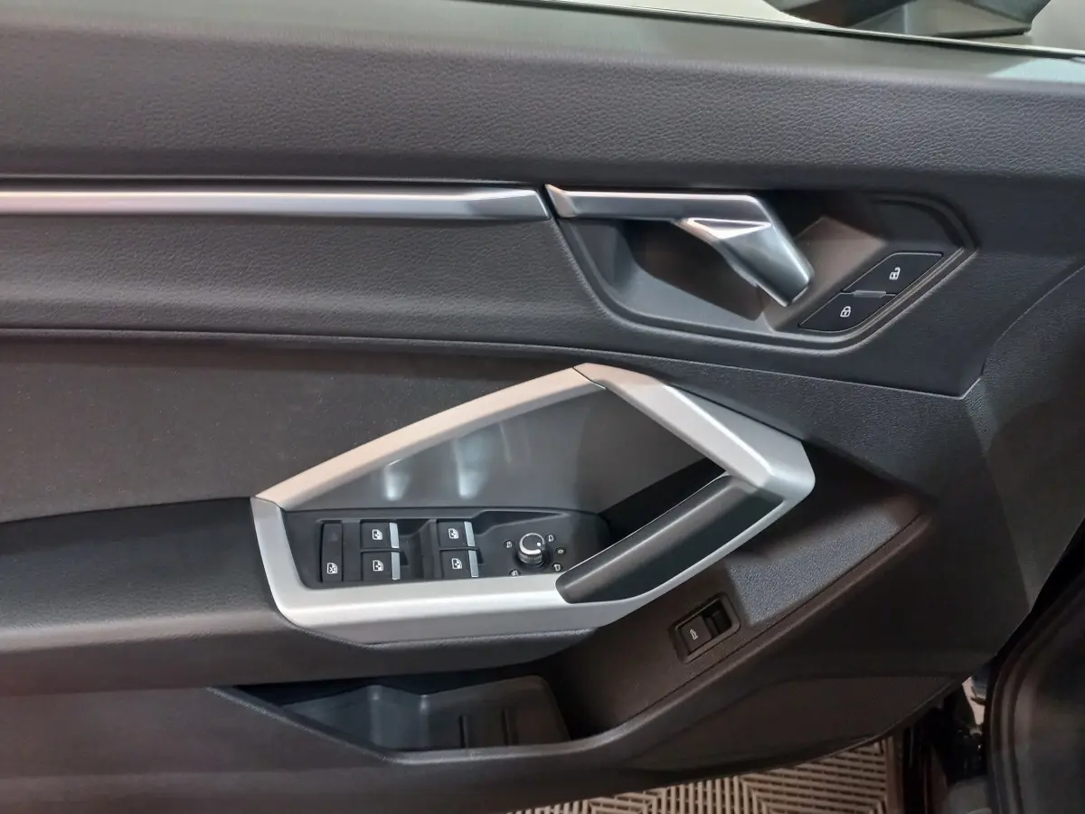 Gros plan sur la porte côté conducteur de l'Audi Q3 Sportback noire, montrant les commandes des vitres et la poignée argentée.