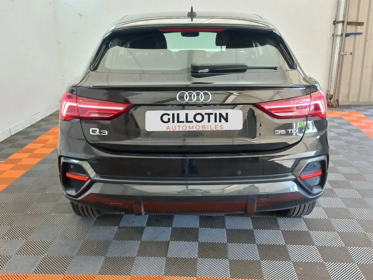 Vue arrière d'un Audi Q3 Sportback noir 35 TDI avec feux LED et logo distinctif sur fond intérieur showroom.