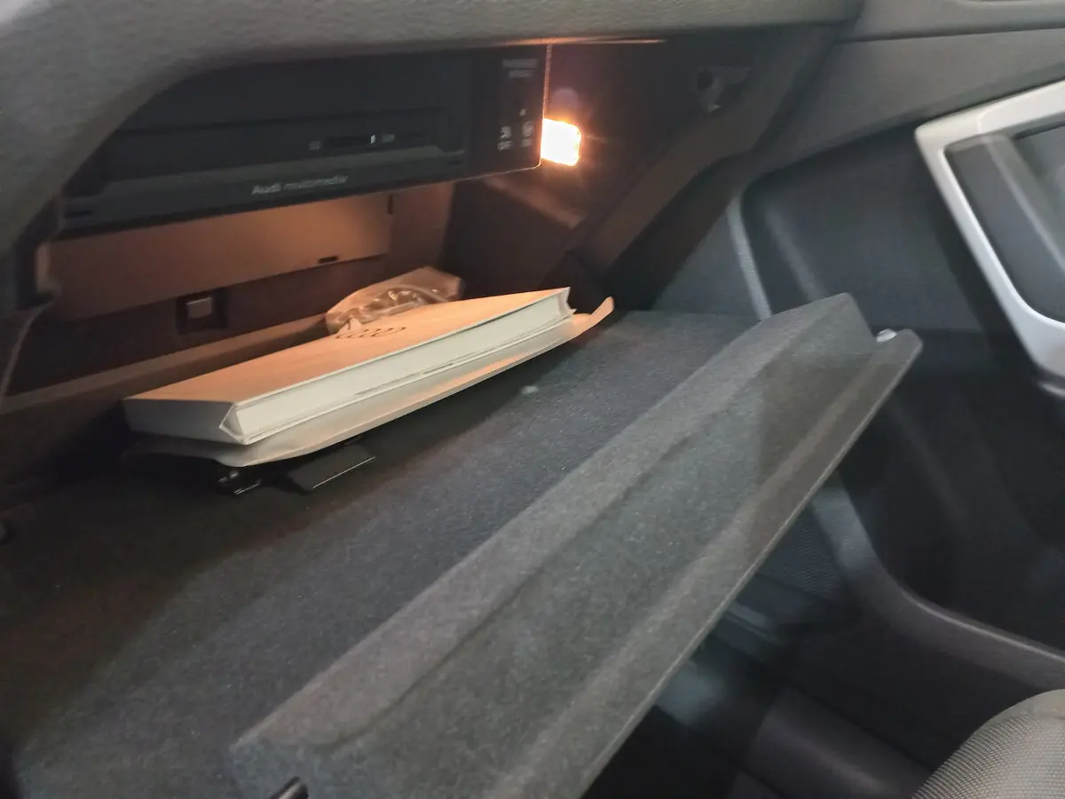 Gros plan sur la boîte à gants ouverte de l'Audi Q3 Sportback 35 TDI noir, avec manuel et éclairage intérieur allumé.