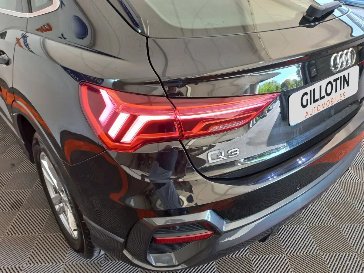 Vue 3/4 arrière droite d'un Audi Q3 Sportback noir avec feux arrière LED allumés et logo Q3 visible.