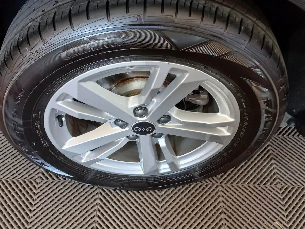 Gros plan sur la jante argentée avec logo Audi d’un Q3 Sportback noir, mettant en valeur le pneu et la roue avant droite.