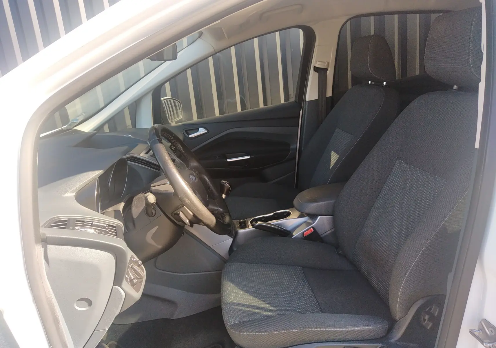 Vue intérieure côté conducteur du Ford C-MAX blanc de 2013, montrant les sièges en tissu noir et le tableau de bord.