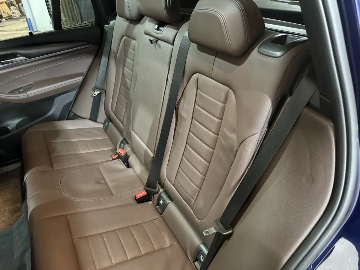 Vue côté droit sur la banquette arrière en cuir marron du BMW X3 xDrive30e bleu, avec ceintures de sécurité visibles.