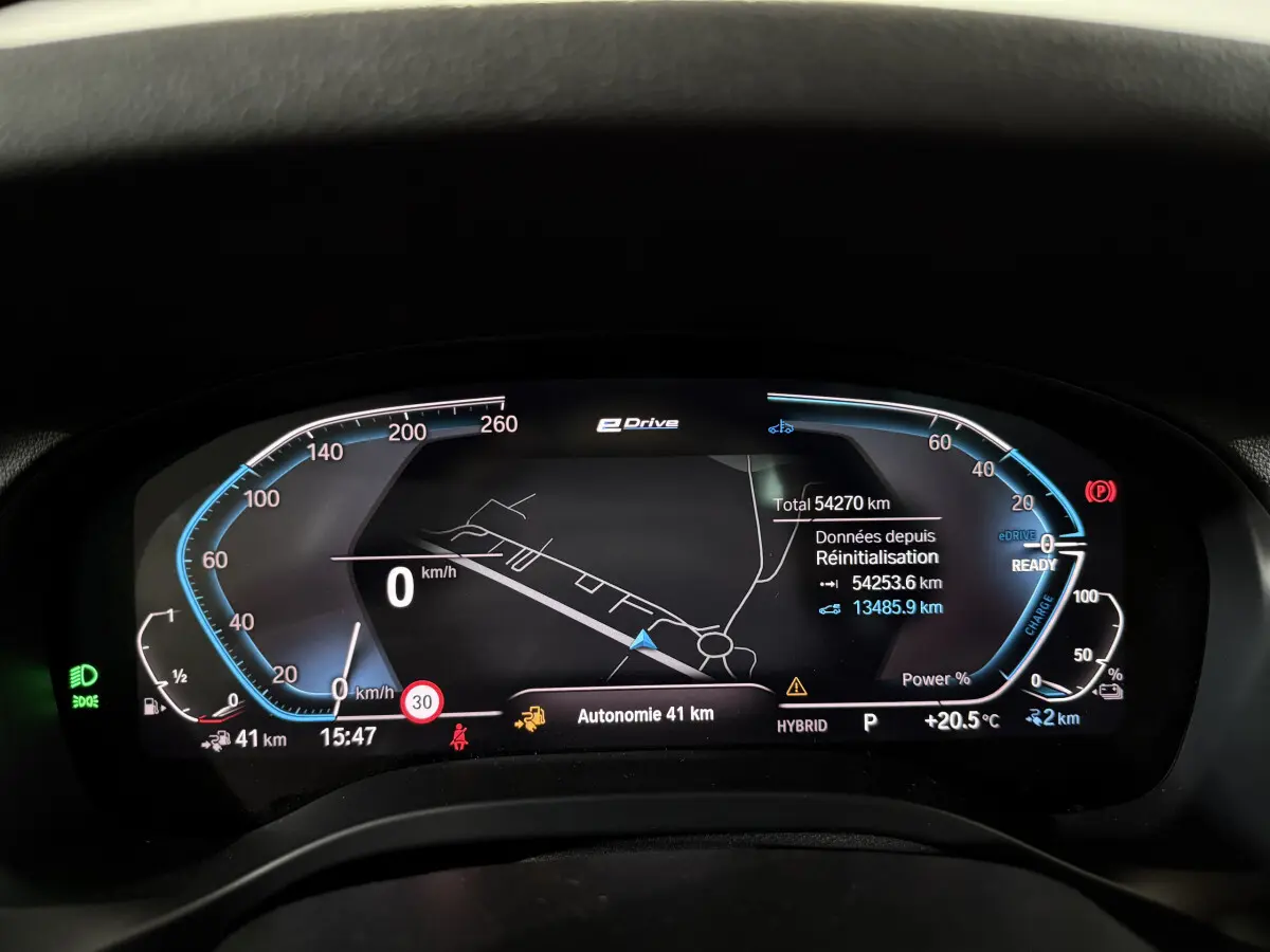 Tableau de bord numérique BMW X3 xDrive30e 2023 affichant la navigation, autonomie et indicateurs hybrides en vue frontale.