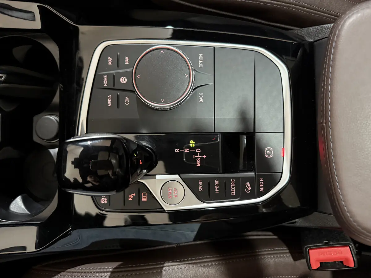 Vue en plongée sur la console centrale noire brillante du BMW X3 xDrive30e avec molette de sélection et levier de vitesse.