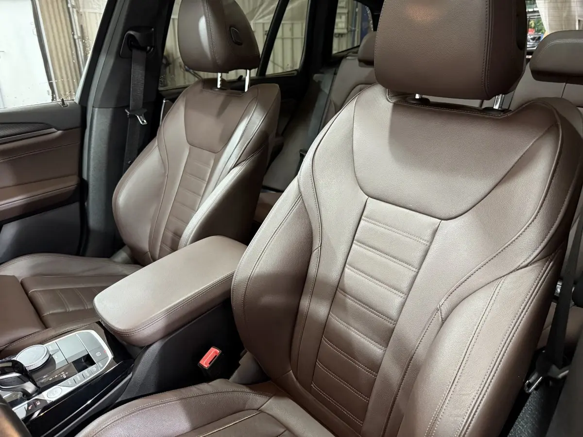 Gros plan sur les sièges avant en cuir marron du BMW X3 xDrive30e 2023, avec accoudoir central et console moderne.