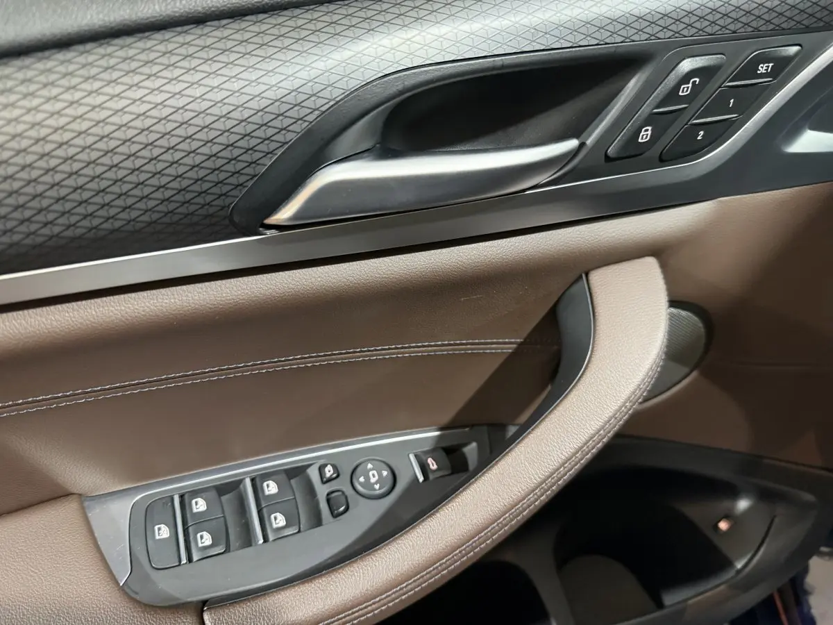 Gros plan sur la porte intérieure côté conducteur du BMW X3 xDrive30e 2023, avec garniture cuir marron et commandes électriques.