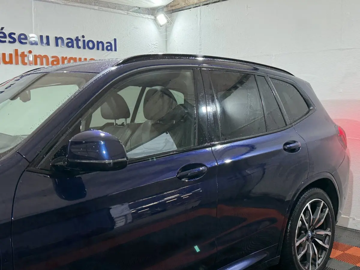 Vue latérale gauche d'un BMW X3 xDrive30e bleu avec jantes alliage et vitres teintées dans un garage.