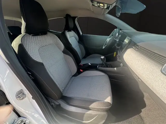 Vue intérieure côté gauche de la Renault Clio V blanche, montrant les sièges textiles gris à motif 3D et la console centrale.