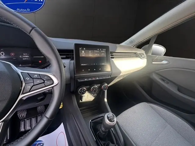 Vue intérieure côté conducteur de la Renault Clio V blanche, montrant volant textile, écran tactile 7'' et levier de vitesse manuel.