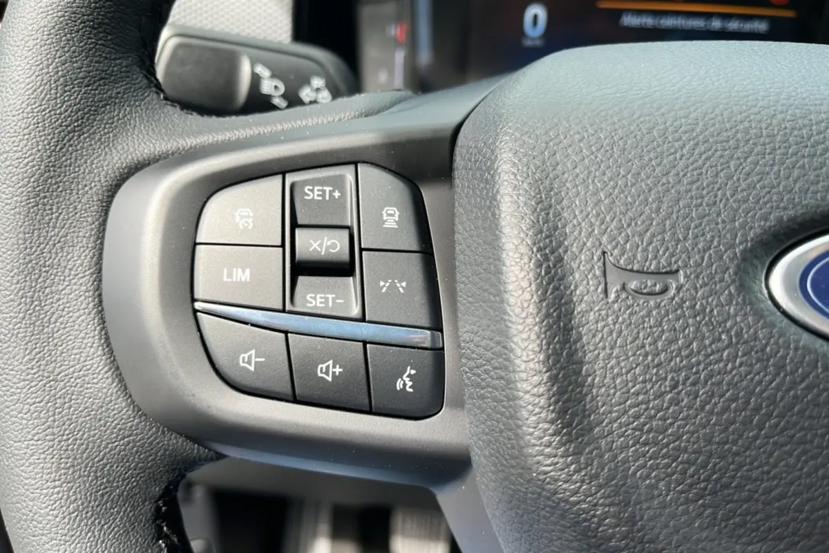 Gros plan sur les commandes multifonctions à gauche du volant en cuir noir du Ford Ranger gris carbone 2025.
