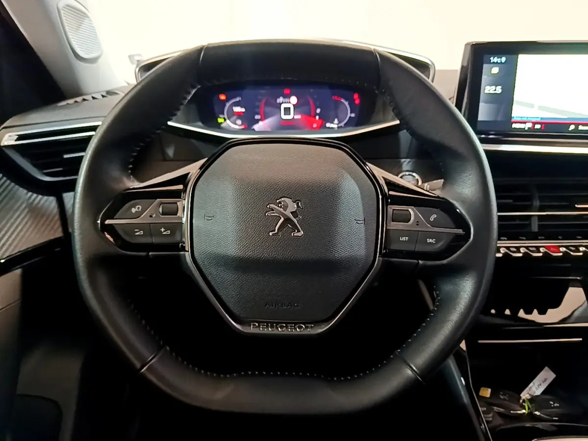 Vue rapprochée du volant cuir noir de la Peugeot 2008 avec commandes intégrées et tableau de bord numérique lumineux.